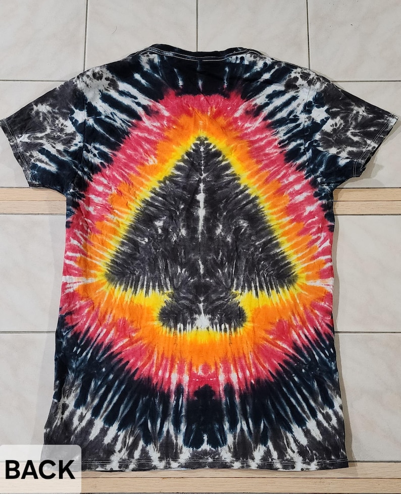 Pu&ograve; includere: Una maglietta tie-dye con un design nero, rosso, arancione e giallo. Il retro della maglietta presenta un motivo centrale a forma di freccia. I colori della maglietta si fondono in un effetto a spirale, creando un aspetto unico.