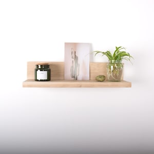 Peut inclure: Une étagère en bois clair avec un pot en verre vert, une impression de cactus, une pierre verte et une plante en pot avec des racines dans l'eau.