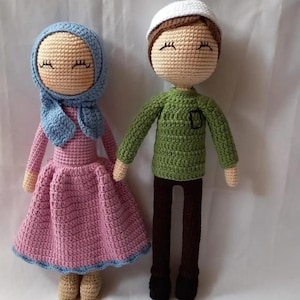 May include: Two crocheted dolls, one wearing a pink dress and a blue headscarf, the other wearing a green shirt and a white hat.
