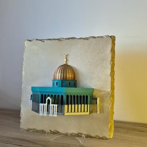 Peut inclure: Un modèle imprimé en 3D du Dôme du Rocher, un célèbre sanctuaire islamique à Jérusalem, monté sur une plaque de pierre. Le modèle est peint dans des tons de vert, d'or et de blanc.