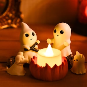 May include: A Halloween-themed display featuring small, white ghost figurines with black eyes and smiling faces. A lit candle sits in a red pumpkin-shaped holder. A small white dog figurine is also present.