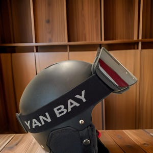 May include: A matte black helmet with a reflective visor and a black strap that reads "YAN BAY" in white lettering. The helmet has a chin guard and is designed for sports or recreational use.