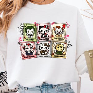 Puede incluir: Una sudadera blanca de manga larga con un estampado gráfico de seis gatos de dibujos animados disfrazados de personajes de películas de terror. Los personajes están etiquetados como The Crazy, Skull Face, Evil Clown, The Slayer, Little Slasher y Masked Camper.