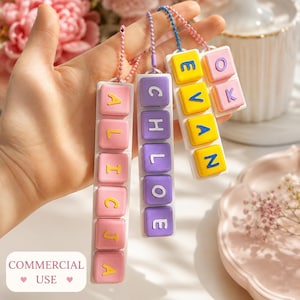 May include: Three vertical keycap-style keychains with ball chains. One pink keychain spells ALICIA with yellow letters. One purple keychain spells CHLOE with white letters. One white keychain spells EVAN OK with yellow and pink letters.