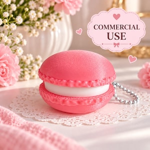 Puede incluir: Un estuche con forma de macarrón rosa con un centro blanco y una cadena de bolas plateada. El objeto presenta una superficie texturizada e incluye una etiqueta festoneada encima con el texto COMMERCIAL USE y pequeños iconos de corazones.