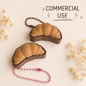 Op de afbeelding: Twee croissantvormige siliconen hoesjes in beige en donkerbruin, elk met een textuur van cirkelvormige patronen. Eén hoesje heeft een donkerbruine kogelketting, de andere een roze kogelketting. De tekst "COMMERCIAL USE" is zichtbaar.