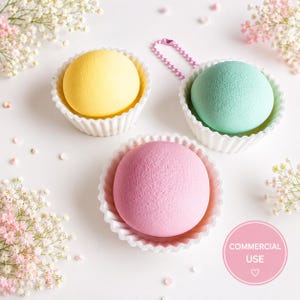 Op de afbeelding: Drie bolvormige sponsjes in pastelgeel, mintgroen en zachtroze, elk rustend in een wit geribbeld papieren cupcakevormpje. Het mintgroene sponsje heeft een klein roze balletjesketting aan de bovenkant. Tekst: COMMERCIAL USE.