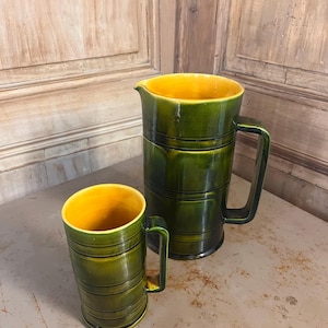 Peut inclure: Ensemble de pichet et de mug en céramique. L'extérieur est vert brillant avec des rainures horizontales, et l'intérieur est jaune vif. Les deux pièces ont une poignée. Le pichet est plus grand que le mug.