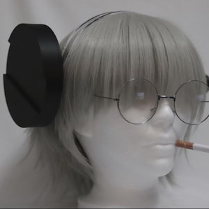 May include: A mannequin head with gray hair, round eyeglasses, and a cigarette in its mouth. The mannequin is also wearing a black accessory on its head, resembling large headphones.