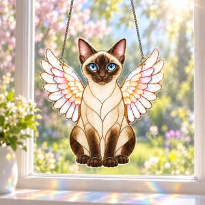 May include: A stained glass suncatcher featuring a Siamese cat with bright blue eyes and large, iridescent white and pink wings. The cat has dark brown ears, face, and paws, with a cream-colored body. It hangs from a thin black metal chain.