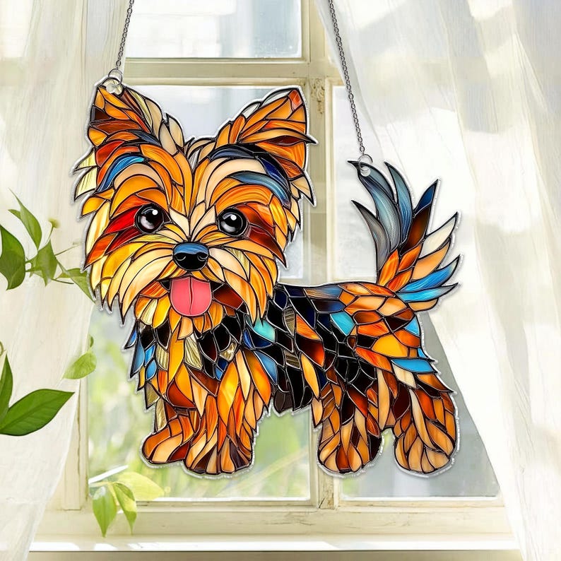 Op de afbeelding: Gebrandschilderde Yorkshire Terrier honden zonnevanger met een kleurrijk moza&iuml;ekontwerp. De hond heeft een roze tong en hangt aan een zilveren ketting voor een raam.