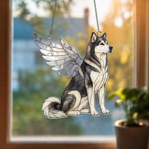 May include: A stained glass suncatcher featuring a sitting husky dog with large, detailed wings. The dog has black, grey, and white fur patterns, and the wings are composed of translucent, segmented glass panels. It hangs from a thin metal chain.