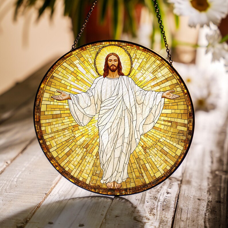 May include: Round stained glass window depicting a figure with outstretched arms, wearing a white robe, and a golden halo. The background is a mosaic of yellow and gold tiles. A black chain is attached to the top for hanging.