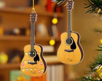 May include: Two guitar-shaped ornaments hanging from a tree branch. One ornament has colorful lights and the name "Emily" written on it. The other ornament has the name "Emily" written on it.