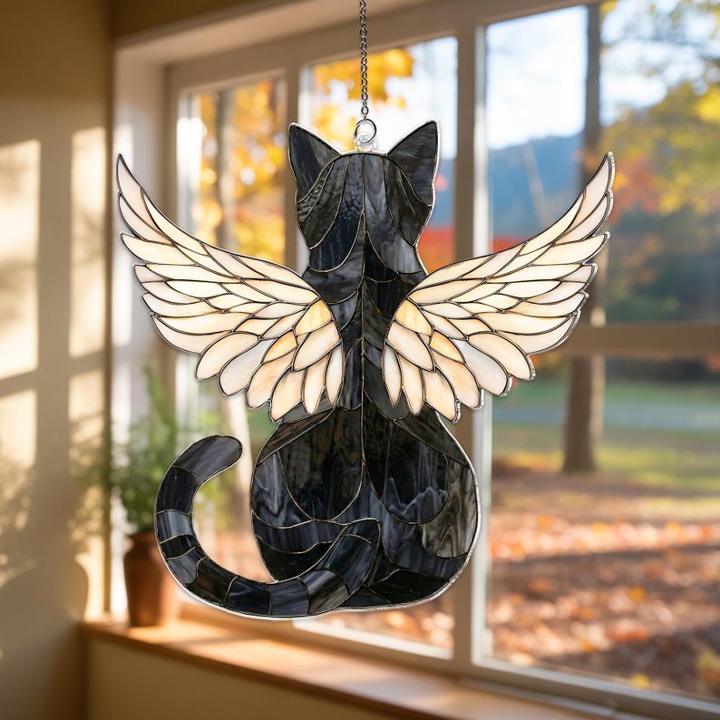 Pu&ograve; includere: Un acchiappasole in vetro colorato a forma di gatto con un corpo in vetro a motivi neri e grigi e grandi ali color crema. Il gatto &egrave; raffigurato di spalle con una lunga coda curva ed &egrave; appeso a una catena di metallo color argento.