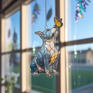 May include: A stained glass dog figurine in shades of blue, gray, and amber, with a butterfly perched on its nose. The dog is suspended by a silver chain, creating a decorative window hanging.