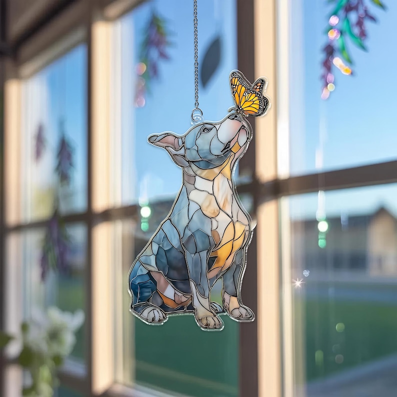 May include: A stained glass dog figurine in shades of blue, gray, and amber, with a butterfly perched on its nose. The dog is suspended by a silver chain, creating a decorative window hanging.
