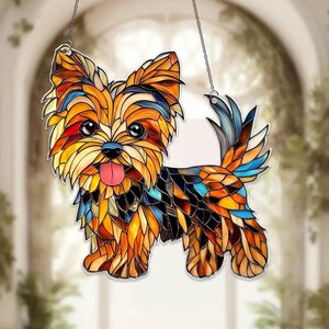Op de afbeelding: Gebrandschilderde Yorkshire Terrier honden zonnevanger. De hond is afgebeeld in moza&iuml;ekstijl met levendige kleuren: oranje, geel, blauw en bruin. Hangt aan een zilveren ketting, ideaal voor raam- of wanddecoratie.