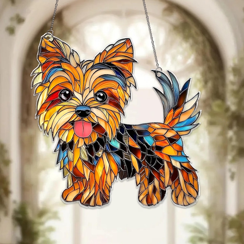 Op de afbeelding: Gebrandschilderde Yorkshire Terrier honden zonnevanger. De hond is afgebeeld in moza&iuml;ekstijl met levendige kleuren: oranje, geel, blauw en bruin. Hangt aan een zilveren ketting, ideaal voor raam- of wanddecoratie.