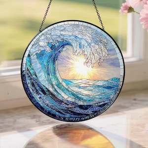 May include: Round stained glass window art depicting a crashing ocean wave with a bright yellow sun in the center. The wave is rendered in shades of blue and white, with a black metal frame and hanging chain.