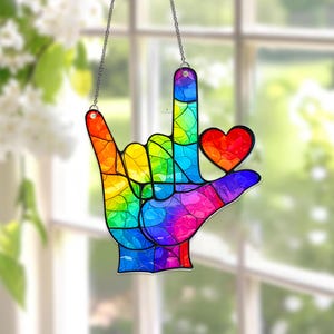 May include: A rainbow-colored stained glass hand in the shape of the American Sign Language symbol for "I love you." The hand has a red heart and is suspended by a silver chain. The colors include red, orange, yellow, green, blue, and purple.