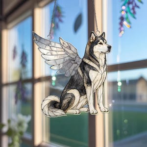 May include: A stained glass suncatcher featuring a sitting husky dog with large, detailed wings. The dog has black, white, and grey fur patterns with defined lines. The wings are translucent with a segmented design. It hangs from a silver chain.