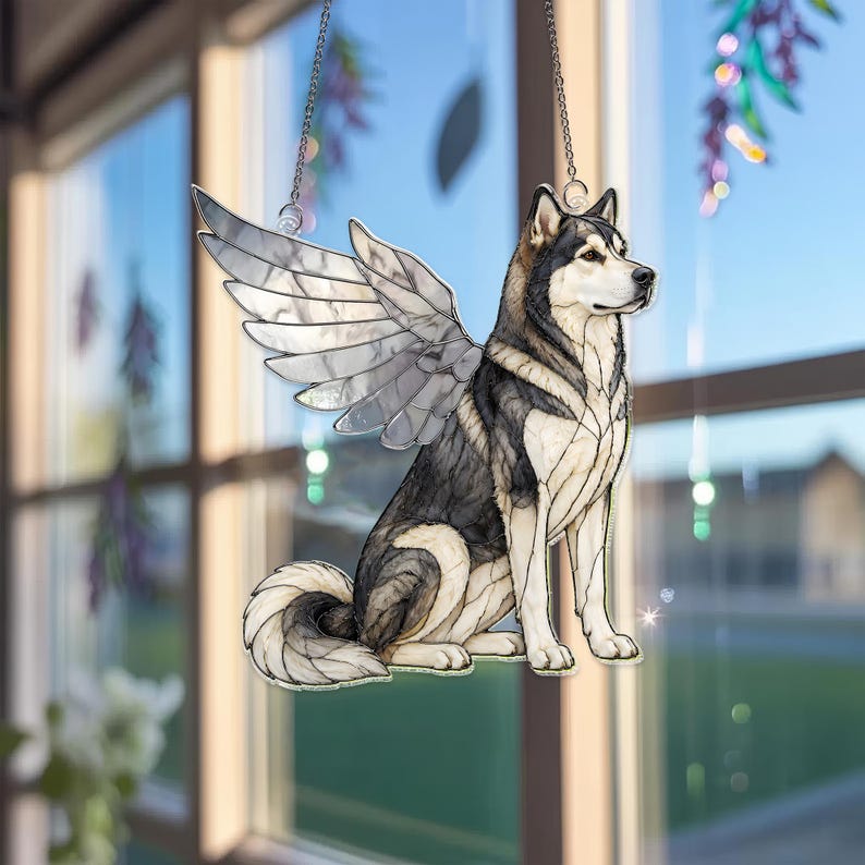 May include: A stained glass suncatcher featuring a sitting husky dog with large, detailed wings. The dog has black, white, and grey fur patterns with defined lines. The wings are translucent with a segmented design. It hangs from a silver chain.
