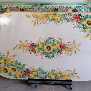 May include: Oval ceramic table top with a white background and a painted floral design. The design features yellow lemons, sunflowers, and red peppers.