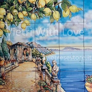 Può includere: Una piastrella in ceramica dipinta a mano che rappresenta una pittoresca scena costiera italiana. La piastrella presenta un albero di limone con limoni gialli maturi, un edificio in pietra con archi, un sentiero tortuoso e una vista del mare con barche. La piastrella è decorata con il testo "Vietri With Love" e l'indirizzo del sito web "vietri.store.it".