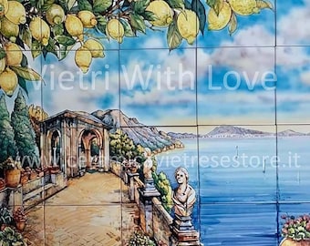 May include: A hand-painted ceramic tile depicting a picturesque Italian coastal scene. The tile features a lemon tree with ripe yellow lemons, a stone building with arches, a winding path, and a view of the sea with boats. The tile is decorated with the text "Vietri With Love" and the website address "vietri.store.it".