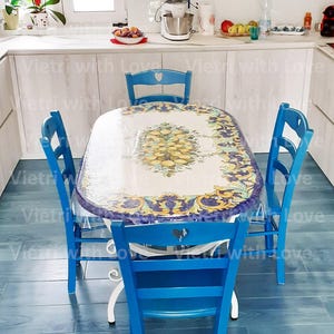 Pode incluir: Uma mesa de cerâmica azul e branca com um design floral e um tampo de vidro transparente. A mesa é cercada por quatro cadeiras azuis com recortes em forma de coração no encosto.