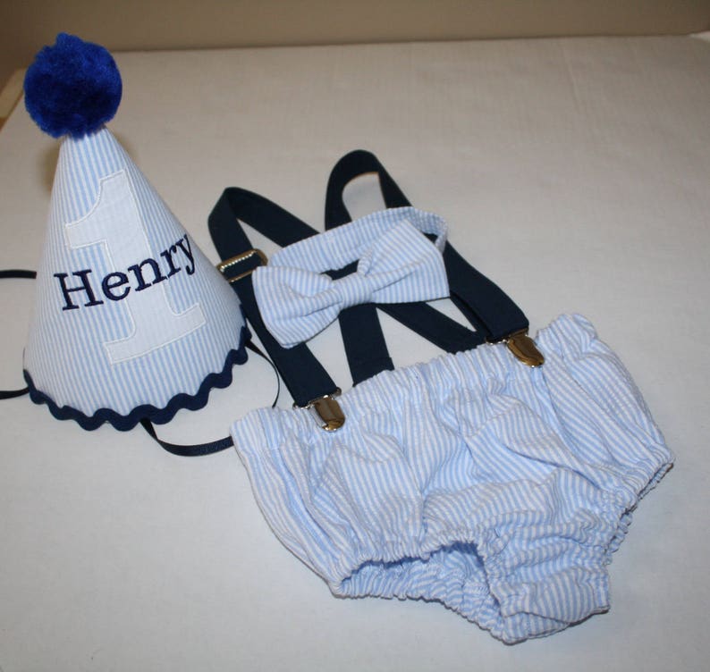 Boys first birthday cake smash outfit. Birthday hat, bow tie, suspenders and diaper cover available.  Personalized birthday hat with number and name. Blue seersucker fabric with navy blue suspenders and hat accents.