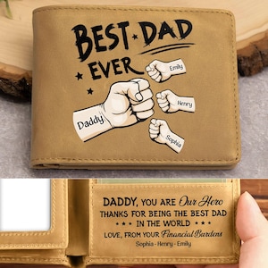 Könnte beinhalten: Ein beigefarbenes, zweifach gefaltetes Portemonnaie mit dem Schriftzug "BEST DAD EVER" und Faust-Illustrationen. Das Portemonnaie trägt die Namen "Daddy", "Emily", "Henry" und "Sophia". Im Inneren des Portemonnaies steht der Text "DADDY, YOU ARE Our Hero..." und die Namen "Sophia - Henry - Emily".