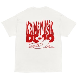 Puede incluir: Camiseta blanca con un diseño gráfico rojo en la espalda. El diseño incluye el texto "KEINEMUSIK DC-10" en una fuente estilizada, junto con un contorno rojo de un avión. La camiseta tiene mangas cortas y cuello redondo.