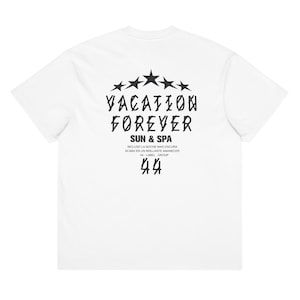 May include: White t-shirt featuring a black graphic on the back. The design includes the words "VACATION FOREVER" above "SUN & SPA", and other text. The shirt also has a star design.