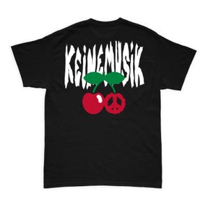 Op de afbeelding: Zwart T-shirt met de witte tekst "KEINEMUSIK" over de schouders. Daaronder een rode kers en een rood vredesteken. De kers heeft groene bladeren.