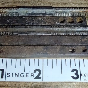 May include: Five metal rods with threaded ends and holes along the sides. The rods are stacked on top of each other and are measured against a white tape measure marked with inches.
