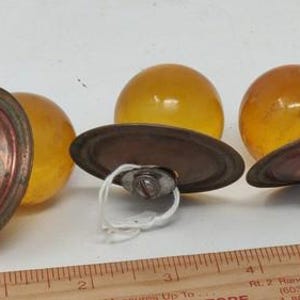 May include: Three antique amber glass knobs with copper-colored metal bases. The knobs have a round, spherical shape and are attached to the metal bases with screws. The metal bases have a circular design.