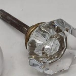 May include: A clear glass door knob with a brass base and a metal stem. The knob has a faceted design.