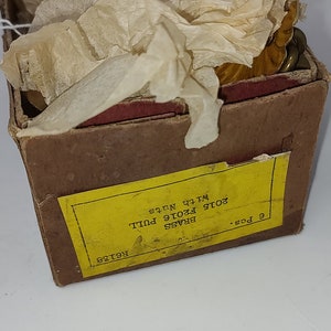 May include: A box of brass pulls with nuts, labeled "2015 F2016 PULL". The pulls are gold-colored and partially wrapped in tissue paper. A US one-cent coin is in the foreground.
