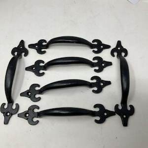 May include: A set of six black metal drawer handles, each featuring a curved grip and decorative fleur-de-lis style ends with pre-drilled screw holes. The handles are arranged in a rectangular formation with two vertical and four horizontal pieces.