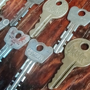 May include: A collection of metal keys, some with the "Master" logo, arranged on a wooden surface. The keys vary in size and design, with visible key teeth and keyholes. The wood has a warm, brown tone.