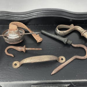 May include: A collection of five antique metal hardware pieces, including a hook, a handle, a screw, and two decorative pieces. The pieces are arranged on a black surface.