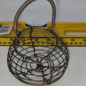 May include: A vintage wire egg basket with a rounded cage design and a curved handle. The basket is made of metal and has a silver finish. The basket is approximately 7 inches in diameter and 8 inches tall.