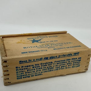 May include: A wooden box with a blue and white label that reads "Choice Boned Salt Hake" and "Royal Star Foods Ltd." The box is labeled as a product of Canada and has a net weight of 454g. The label also includes instructions on how to prepare the fish for cooking.