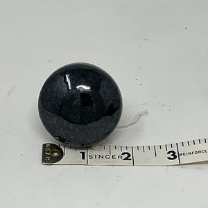 May include: A dark, glossy, spherical object, possibly a decorative knob or sphere. The object is black with subtle variations in color. A measuring tape is placed next to the sphere, showing a diameter of approximately 2 inches.