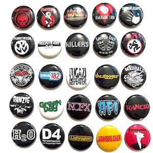 May include: A collection of 25 round, black pinback buttons featuring band logos and names. The buttons display various colors and graphics, including text and illustrations. Bands include The Offspring, Blink 182, and Rancid.