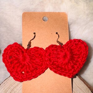 Puede incluir: Un par de pendientes de corazón de ganchillo rojo con ganchos dorados.
