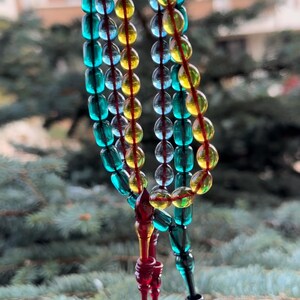 Puede incluir: Tres hebras de cuentas de oración de colores, con cuentas azules, verdes, amarillas y rojas. Las cuentas están enhebradas en un cordón y tienen un borla al final.