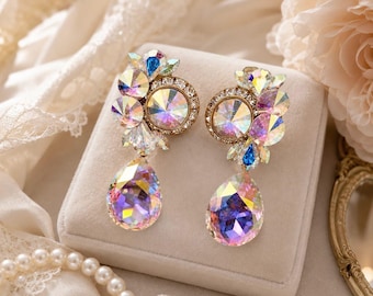 May include: A pair of statement earrings featuring clusters of iridescent, multi-faceted crystals in circular and teardrop shapes. The crystals display a spectrum of colors including pink, blue, and gold, set in a metallic frame with small clear stones.